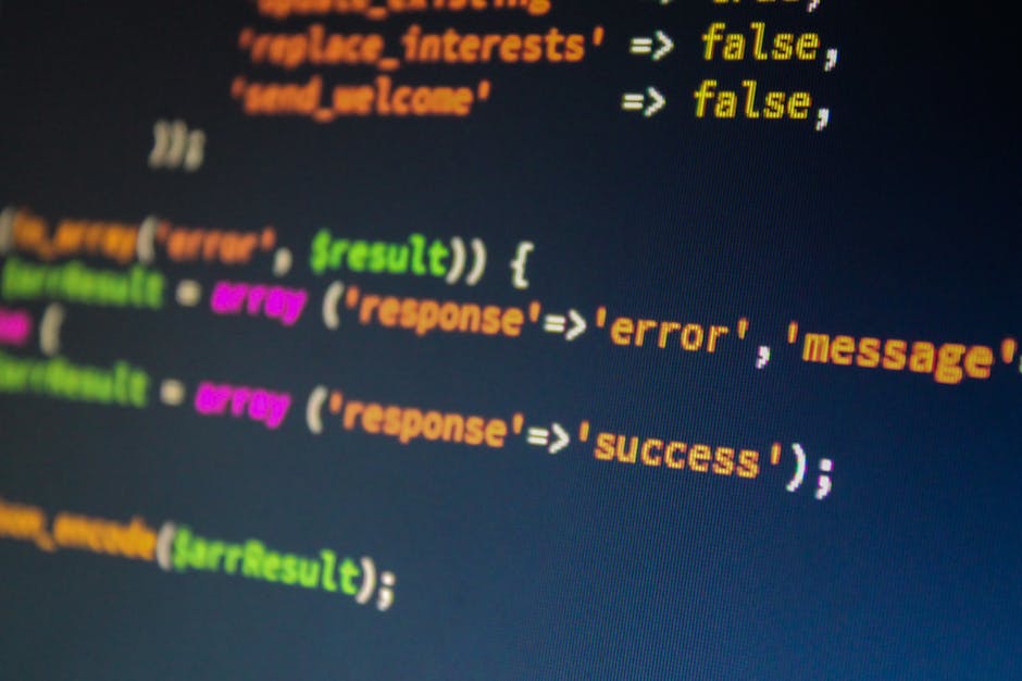 A close-up image of a computer screen displaying colorful lines of programming code with syntax highlighting in shades of orange, green, pink, and yellow on a dark background. The code appears to be p
